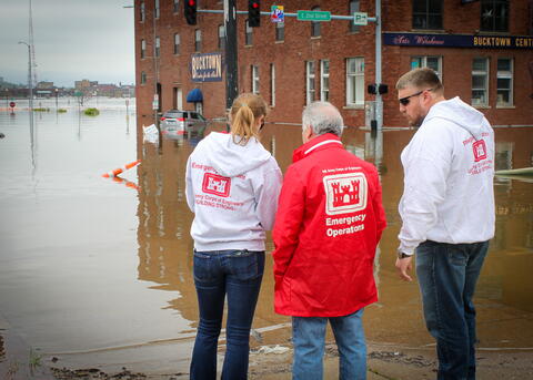 Elizabeth Bruns stands with two other individuals beside a flooded street. 