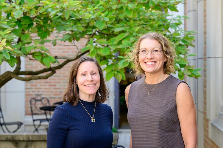 Jacinda Dariotis (left) and Amy Leman Two women smiling at the camera, standing outdoors in front of a building and a tree